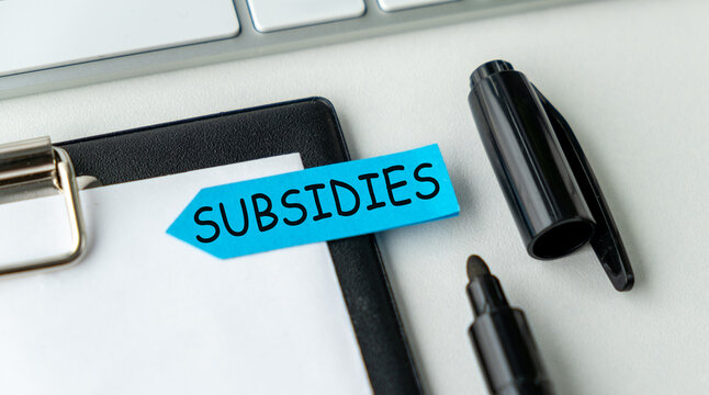 A blue sticky note with the word Subsidies written on it is on top of a clipboar