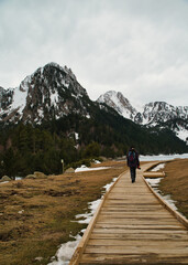 A young hiker walks across a wooden bridge over a stream in Aigüestortes and Estany de Sant Maurici National Park, in the Spanish Pyrenees, surrounded by mountains.