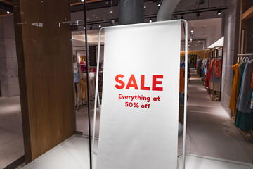 Red SALE sign inside modern fashion store with clothing racks and in store discount promo