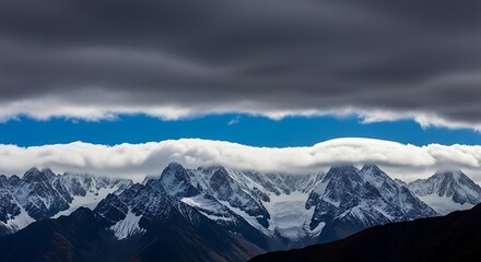 Obraz premium Dramatic mountain range with snowcapped peaks under a stormy sky, creating a captivating contrast of light and shadow in a breathtaking alpine landscape