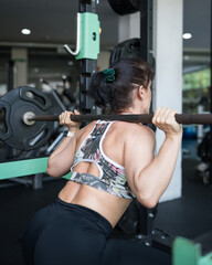 Woman exercising squatting with barbell in gym