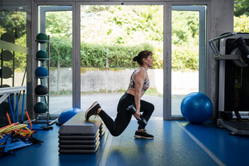 Woman exercising with dumbbell doing lunges at gym