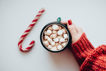Woman in knitted red sweater holding cup of hot chocolate with candy cane.