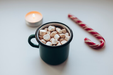 Mug with hot chocolate or cocoa with marshmallow, candy cane and candle.