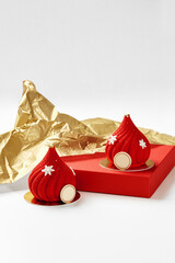 Two red christmas mousse cakes decorated with snowflakes and gold details resting on red surface with gold wrapping paper
