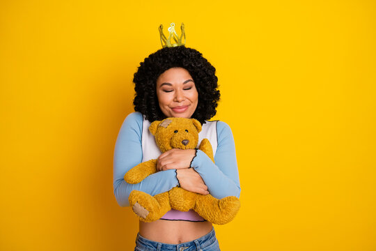 Fototapeta Smiling young woman in casual outfit hugging a teddy bear with joy against a vivid yellow background