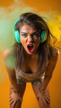 Femme fatale sur fond orange &eacute;nergique avec de la poussi&egrave;re verte, argent&eacute;e, blanche et une &eacute;paisse fum&eacute;e festive, portant un casque audio, les mains sur les genoux et criant.