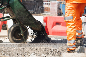 Construction worker pours asphalt from a wheelbarrow during road repair in urban area on a sunny day