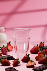 Pink background with empty glass and strawberries
