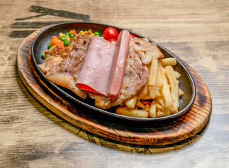Sizzling Mixed Steak Grill Platter Chicken, Ham, Sausage, Fries and Veggies served on a hot cast iron skillet over a wooden board side view