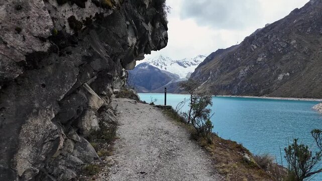 Huaraz, Peru: Point of view of a traveler walking on the trail by laguna paron in Huaraz, Peru. Located in Cordillera blanca mountain with dramatic sky over snowcaped Piramide mountain peak 