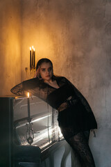 Mysterious woman in black lace poses with a candle in a smoky, gothic setting beside a vintage piano.