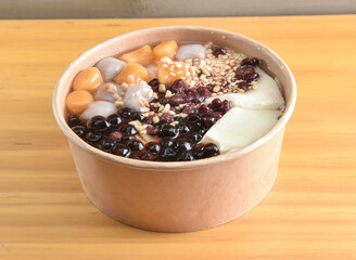 Traditional Tofu Pudding Douhua Dessert with Rich Malt Candy Syrup, Taro Balls, Red Beans, and Peanuts in bowl on wooden table side view of Asian Dessert