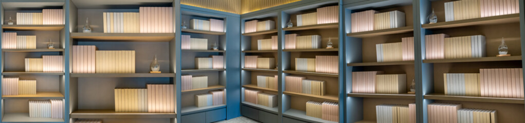 a minimalist bookshelf with four wooden shelves, each containing neatly arranged, vertically aligned, pastel pink and beige books. The shelves are illuminated from within, casting a warm glow