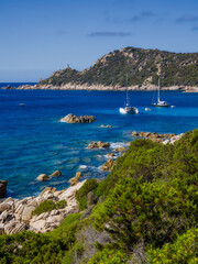 Obraz premium the bay of Cap Muro with its beautiful turquoise water, boats at anchor, and the lighthouse on the hill in sunshine and blue skies