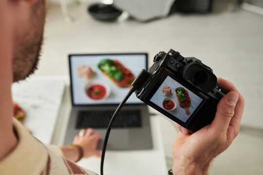 Man photographing food with digital camera while reviewing image on laptop, capturing overhead shot of meal for content creation or food blogging project