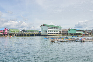 Fototapeta premium PHUKET, THAILAND - 12 NOVEMBER 2017: Coastal village with stilt buildings and calm waters under cloudy sky.