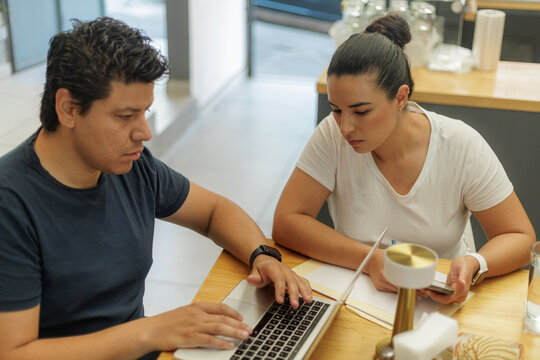 Jóvenes profesionales colaborando en un proyecto con laptop y cuaderno en un entorno de oficina moderno.