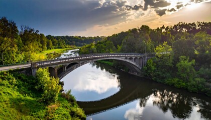 Obraz premium Stone bridge spans river under cloudy sky during golden hour