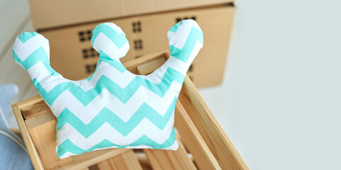 Blue zigzag crown pillow in wooden crate with cardboard boxes in soft nursery room.