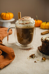 Pumpkin spice latte in glass mug with whipped cream and cinnamon, autumn hot drink