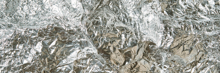 Crinkled aluminum foil texture with reflective shiny silver surface and abstract patterns.