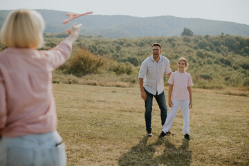 Family enjoys a sunny day flying a toy airplane in a green field with mountains in the background during the afternoon