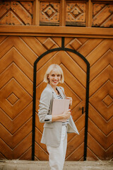 Woman with a folder smiles in front of a wooden door in a sunny location