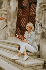 Young woman enjoying a book on the steps of an old building in a sunny location