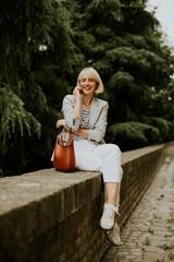 Woman talking on the phone while sitting on a stone wall surrounded by trees