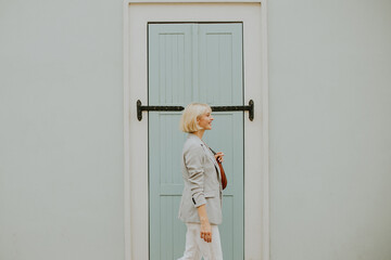 Woman walking by a light blue door while carrying a small bag during a sunny day in an urban area