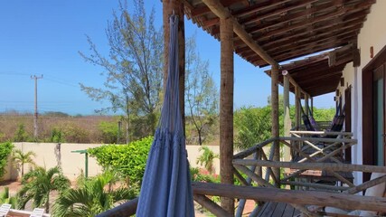 Tropical guesthouse balcony with hammocks, rustic wooden railings, lush green plants, and blue sky. Relaxing accommodation, holiday vibe, tranquil nature retreat in Brazil.