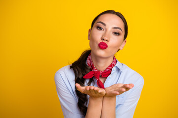 Smiling young woman blowing kisses wearing red bandana and casual shirt on yellow background