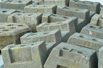 A close-up horizontal shot of numerous stacked grey concrete interlocking pavers with a weathered texture. These are ready for use in paving projects, ideal for landscaping or roadworks.