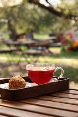 Hot drink, mulled wine or berry tea in a glass cup, waffle cake with condensed milk. Non-alcoholic mulled wine and cake in a wooden tray. Hot drink and dessert close-up. Food on the veranda of a cafe