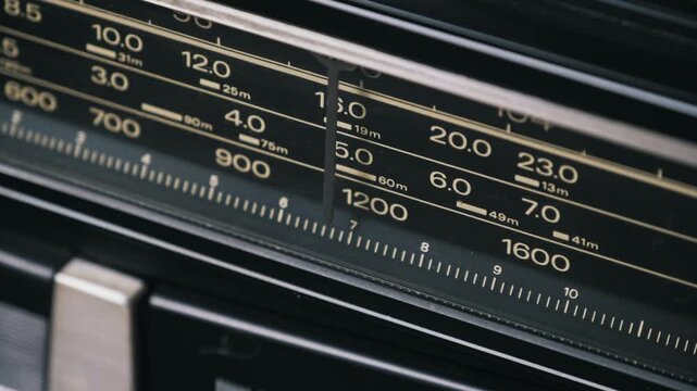 Angled macro of a radio tuner indicator moving across an analog frequency scale searching for stations on a vintage boombox showing MW and SW bands with white numbers on a black plastic display