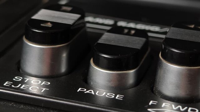 Macro shot of a finger pressing the pause button on a vintage cassette tape player deck showing the textured silver and black key with white text stopping the analog audio media playback
