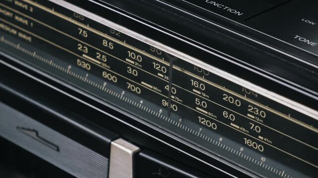 Macro shot searching radio frequencies on a vintage tuner with an indicator scanning across a black analog scale showing yellow numeric markings for MW and SW bands on a classic 80s ghettoblaster