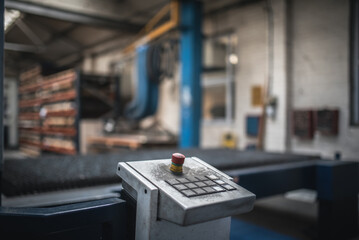 A close-up view of an industrial control panel with a prominent red button and a blurred factory background.