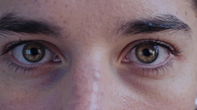 Extreme close up shot of a young person's beautiful hazel eyes. A steady, focused gaze looks directly into the camera, blinking softly