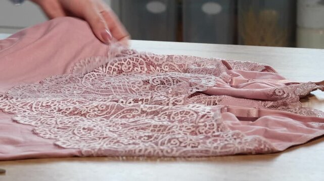 A woman is reviewing a pink lace nightgown. She is laying it out on the table