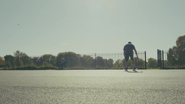 A skateboarder doing tricks in slow motion in a basketball pitch in the sunset