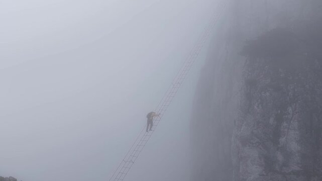 Hiker climbing a long suspension bridge ladder in heavy fog, Dachstein, Austria