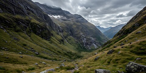 Dramatic view of a deep, green mountain valley with cloudy skies and rocky slopes.