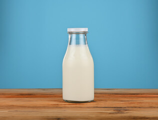 Glass milk bottle standing on wooden table with blue background