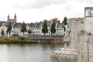 Fototapeta premium Autumn Scene Along Maastricht Riverfront With Historic Buildings And Sculpted Stone Bridge By Calm Waterfront Quays
