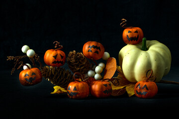 Festive Halloween still life with small pumpkins, jack-o'-lantern faces, autumn leaves, and berries on a dark background