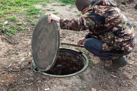 A man lifts a manhole cover to access an underground sewer system. Servicing septic tanks and rural cesspools