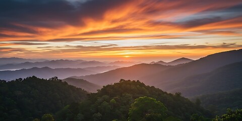A breathtaking sunrise paints the sky with orange and purple hues over layers of misty mountain ranges covered in dense forest.