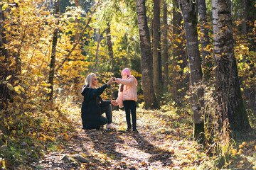 A loving mother and her young daughter share a happy moment on a sunlit path in a golden Estonian autumn forest.